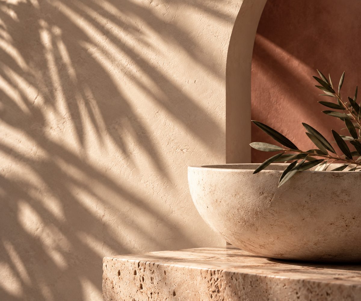 Art direction study: an olive branch resting in a stone bowl beneath a plaster arch, wrapped in warm shadow